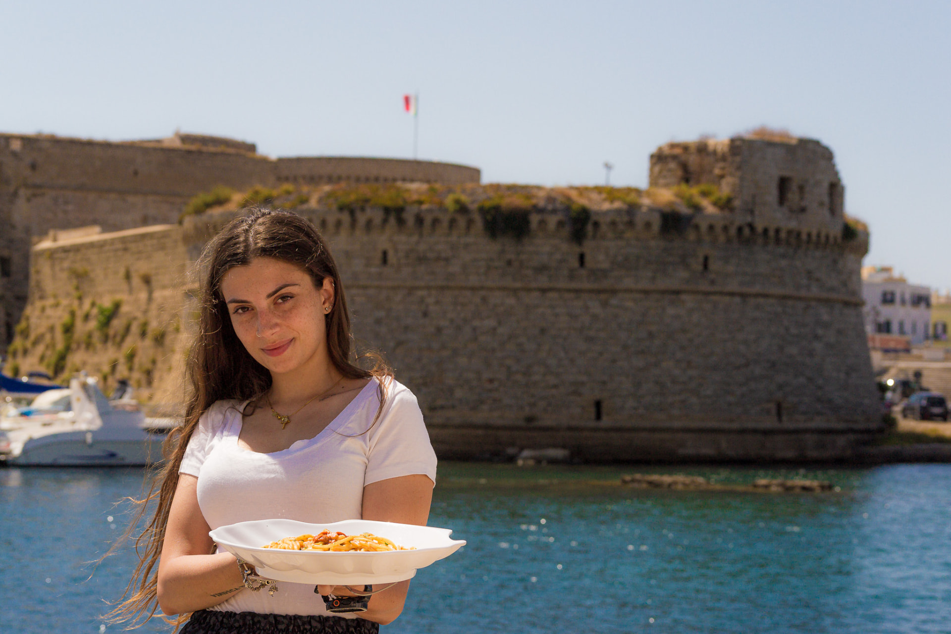 Giada dello staff Costa del Sud con un piatto di pasta ai frutti di mare davanti al castello di Gallipoli